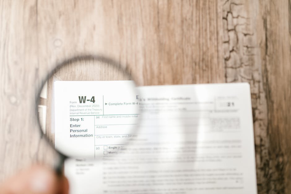 Close-up of a W-4 tax form through a magnifying glass on a wooden table.
